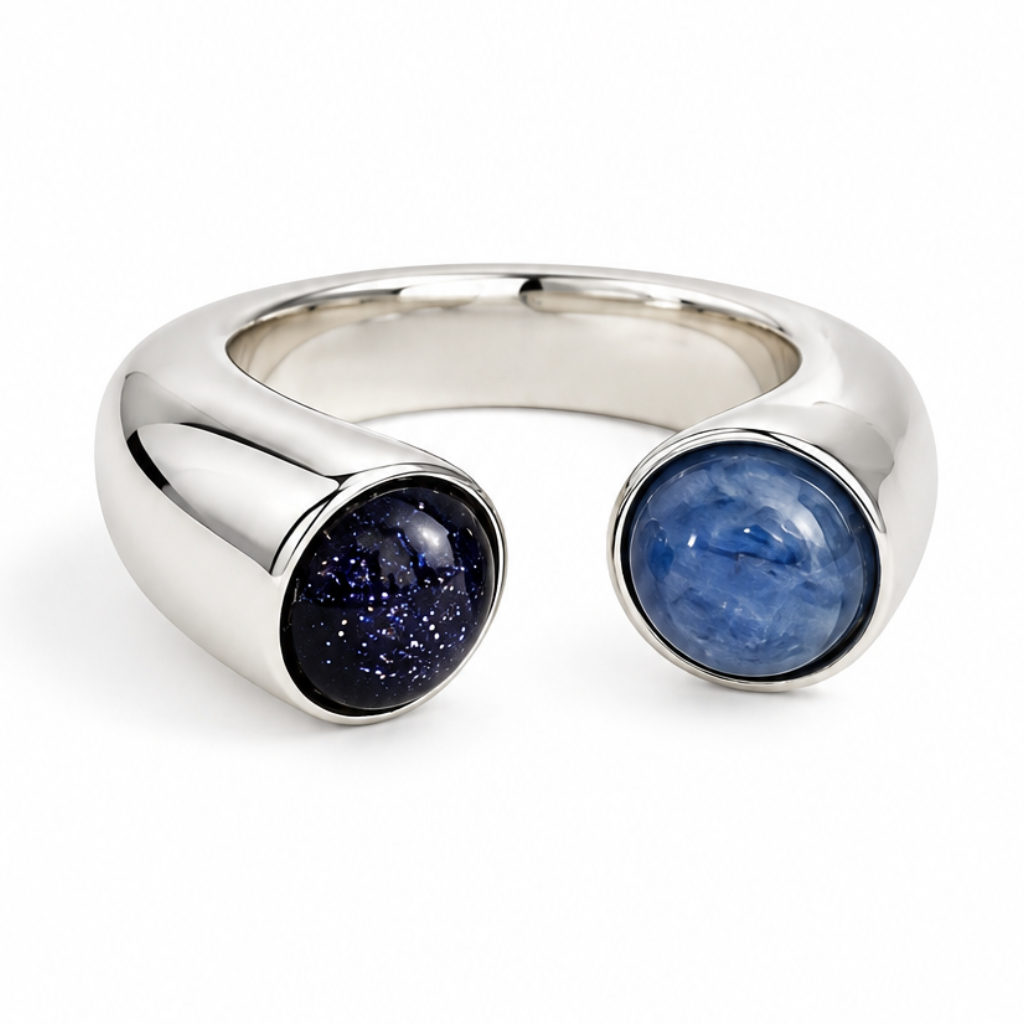 A silver-toned open cuff ring featuring two round bezel-set stones, one dark blue with fine glitter and the other a solid medium blue, shown on a plain white background.