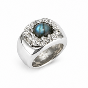 A silver-toned ring featuring a round iridescent blue-green center stone surrounded by a halo of small clear stones, set on a plain white background.