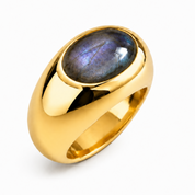 A polished gold signet-style ring featuring an oval cabochon gemstone with a blue-purple iridescent luster, set against a clean white background.