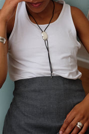 Person wearing a white tank top and gray skirt with a necklace.