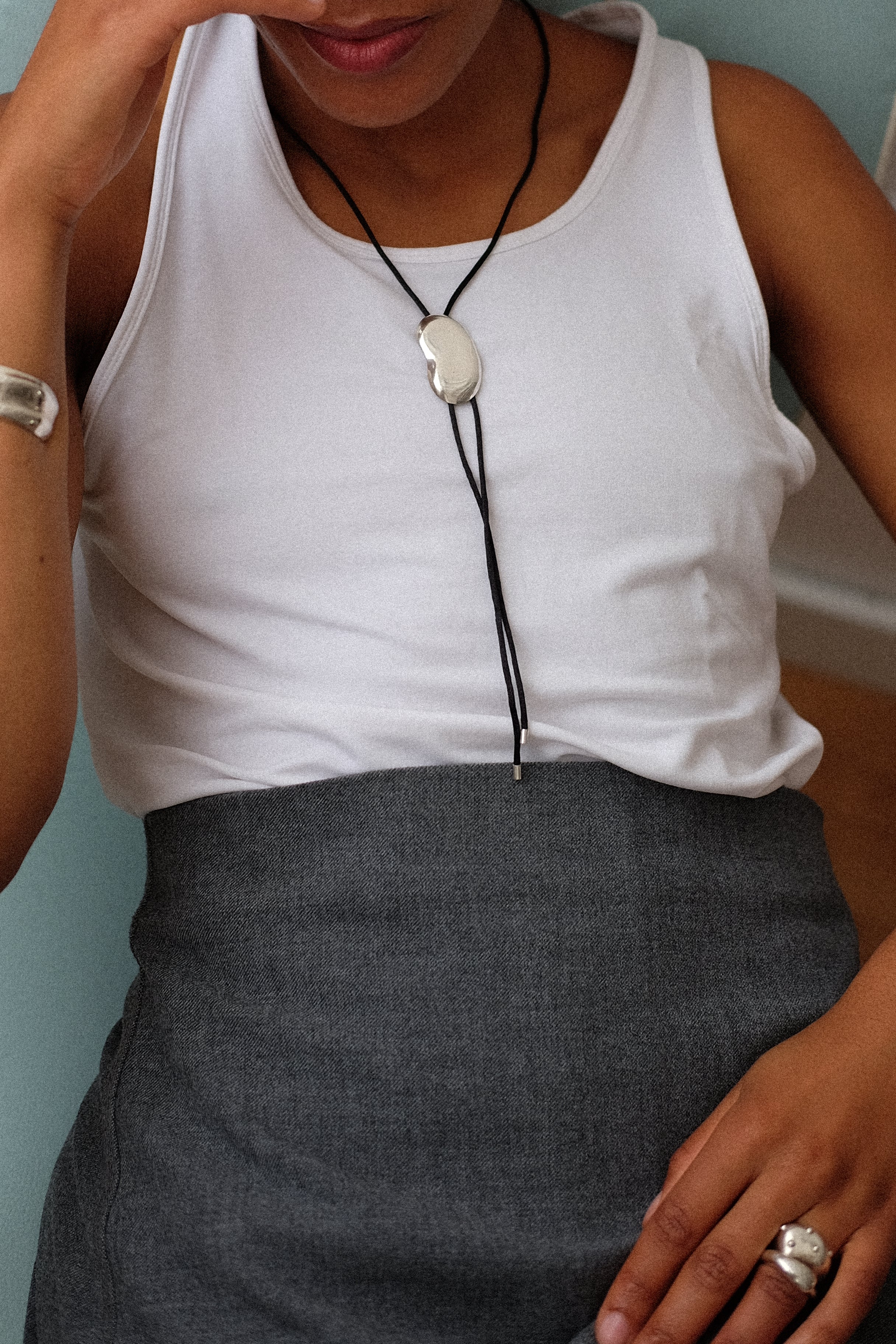 Person wearing a white tank top and gray skirt with a necklace.